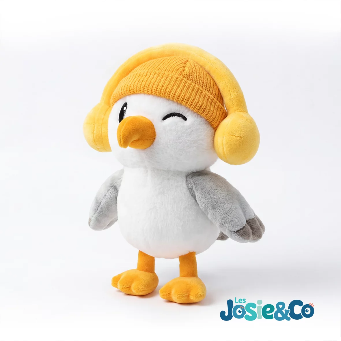 Peluche Josie la Mouette debout sur ses pattes palmées, un clin d'œil sous son bonnet jaune